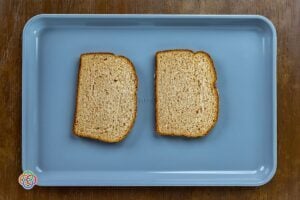 Two slices of wholemeal bread placed on a baking tray, ready for toasting in the oven as part of a baked egg and cheese toast recipe.