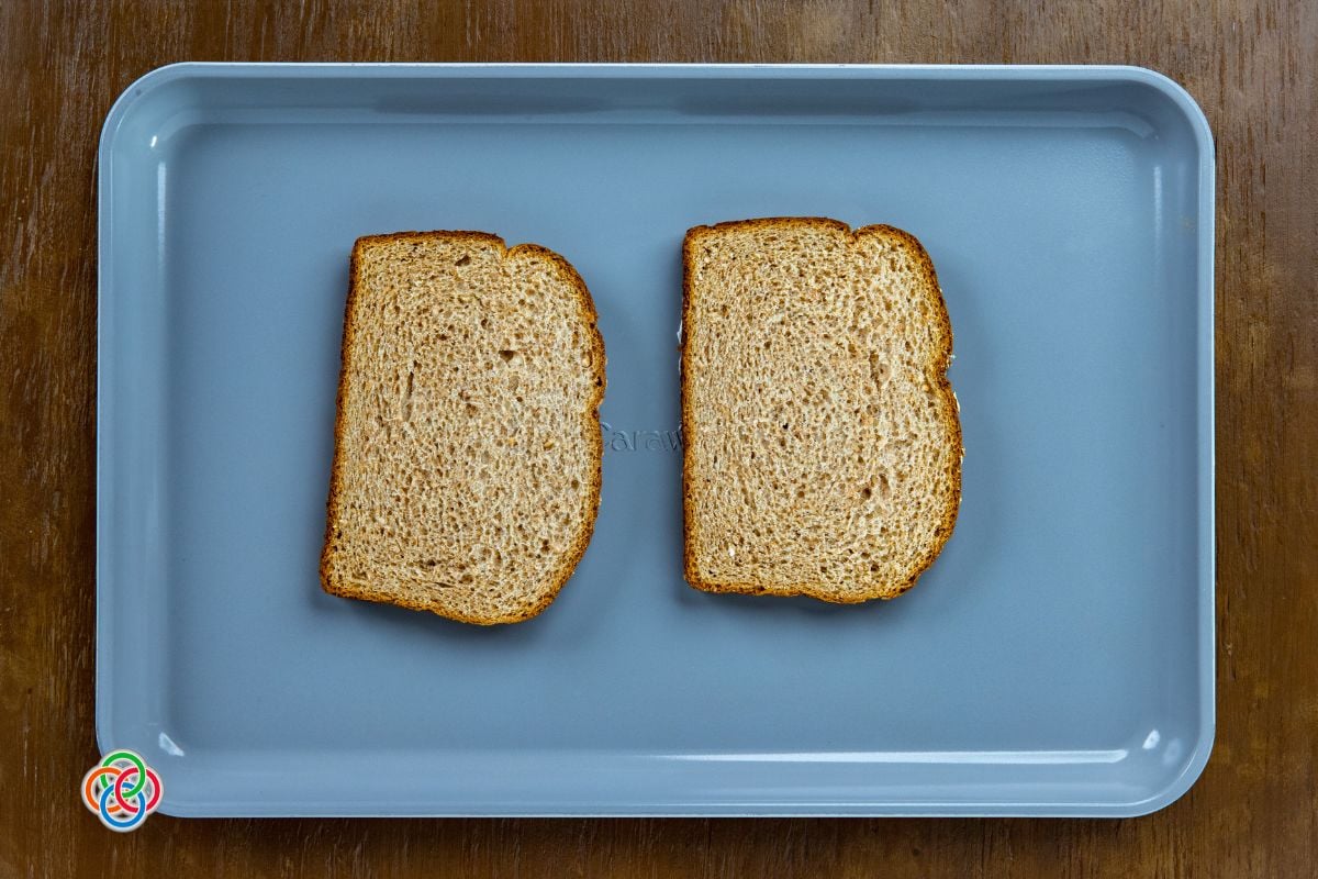 Two slices of wholemeal bread placed on a baking tray, ready for toasting in the oven as part of a baked egg and cheese toast recipe.