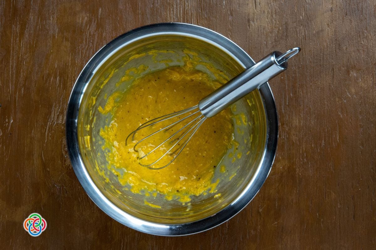 A bowl of whisked egg and cheese mixture with seasoning and a whisk, prepared for making baked egg and cheese toasts.