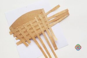 Paper Easter basket base with brown strips woven across in an over-under pattern, with extra strips extending from the sides before trimming.