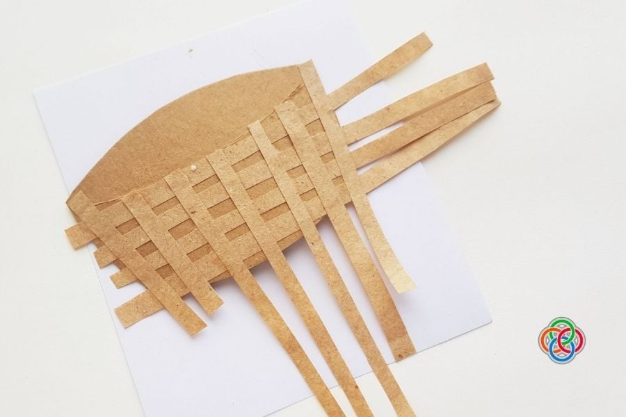Paper Easter basket base with brown strips woven across in an over-under pattern, with extra strips extending from the sides before trimming.