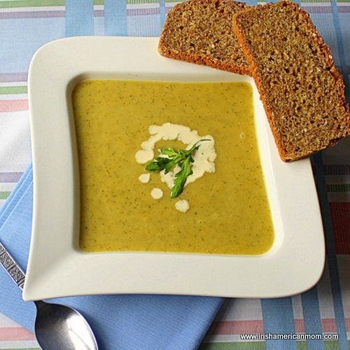 A bowl of pale green zucchini and leek soup served with brown bread.