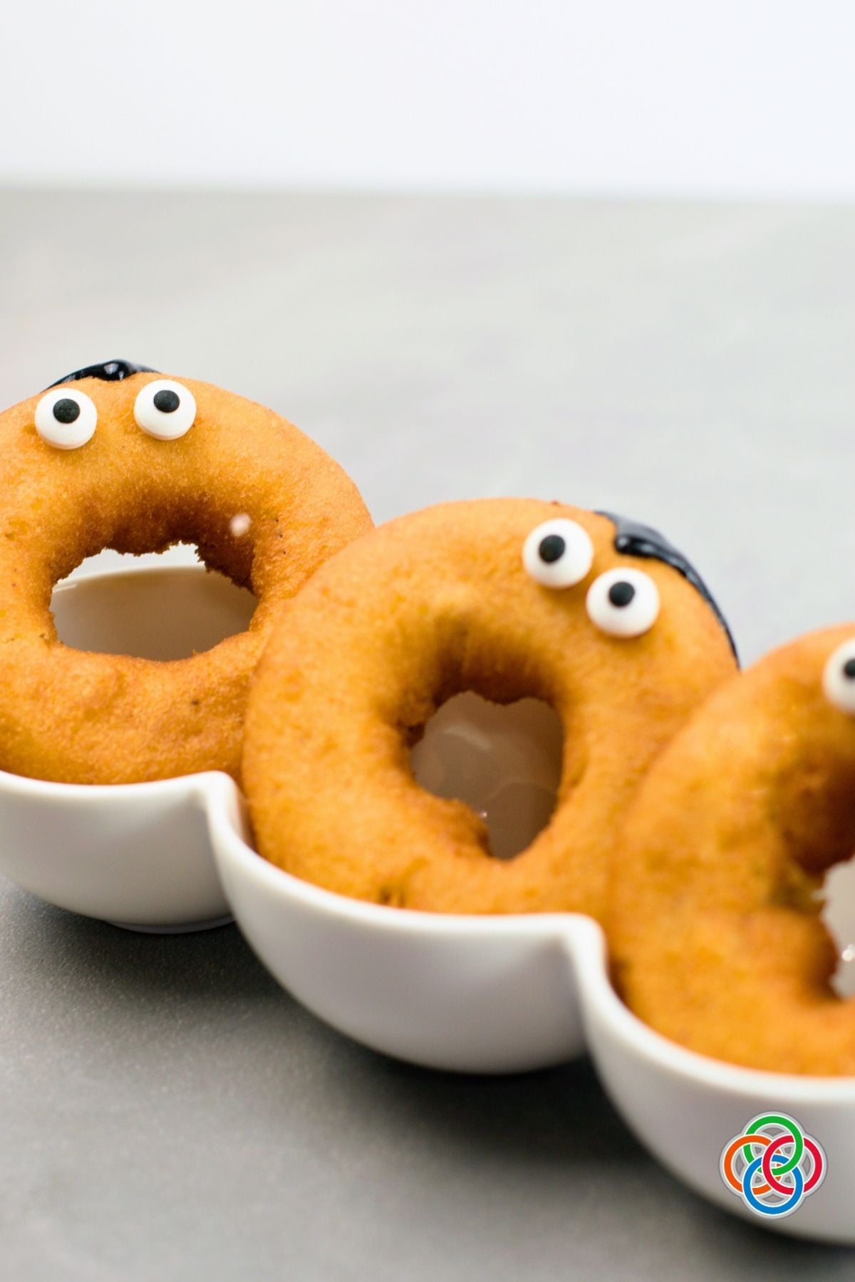 Plain golden donuts decorated with candy eyeballs and black icing hairlines as part of an easy Dracula donut Halloween decorating project.