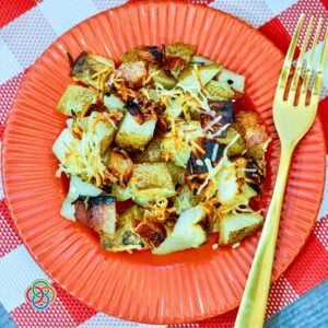 Bacon Parmesan Sheetpan Potatoes | Irish American Mom Roasted Bacon Parmesan Sheet Pan Potatoes with crispy bacon, garlic and golden Parmesan cheese served on a red plate with a gold fork.