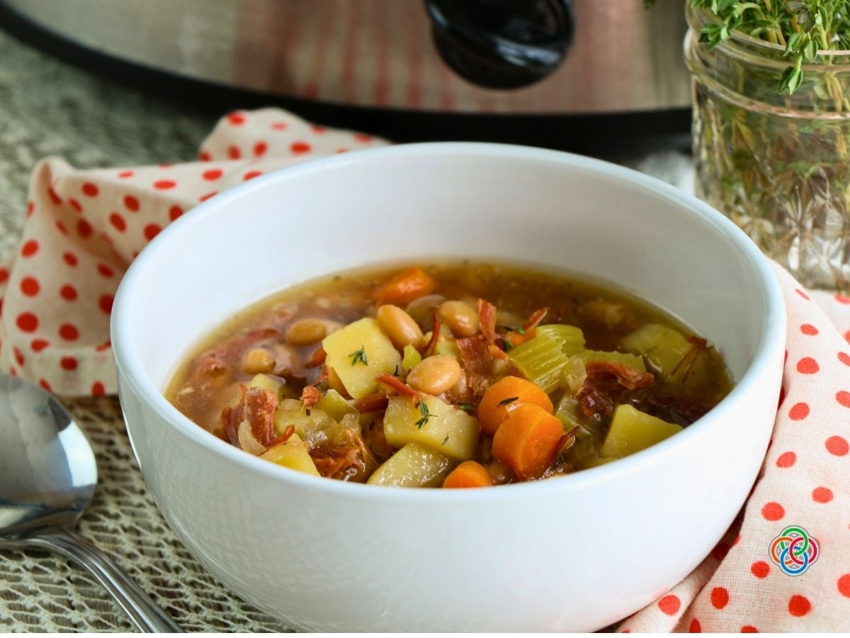 Bowl of homemade ham bone soup | Irish American Mom White bowl of homemade slow cooker ham bone soup filled with shredded ham, potatoes, carrots, celery and white beans in a savory broth.