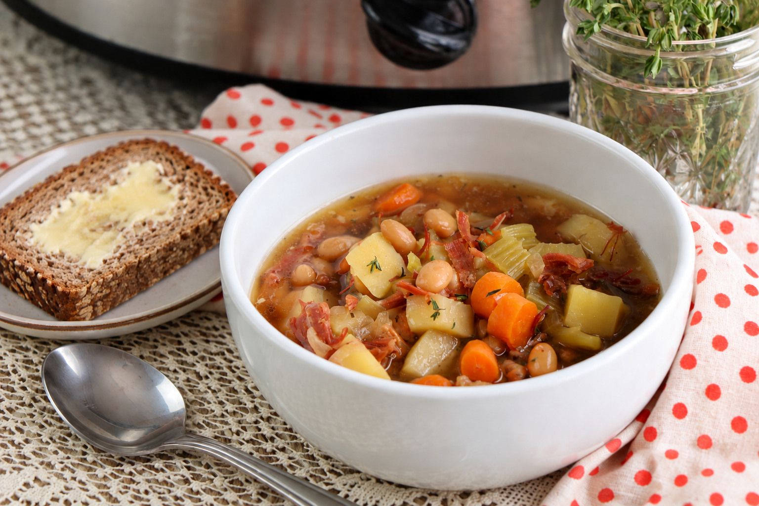 Brown bread and ham bone soup | Irish American Mom A bowl of ham and vegetable soup with a spoon and a slice of buttered wholewheat bread on a plate.