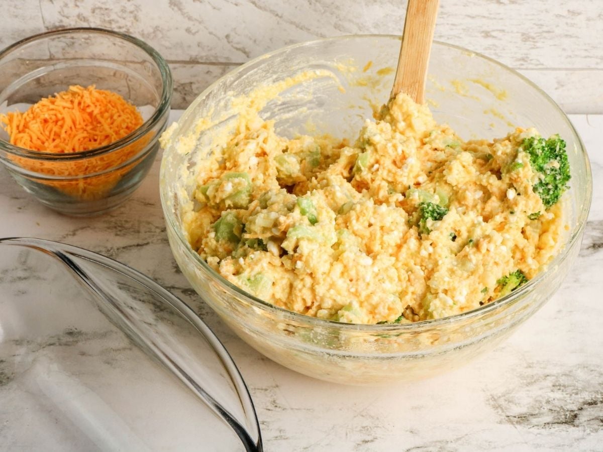 Cheddar broccoli cornbread batter in a bowl | Irish American Mom Thick cheesy cornbread batter mixed with broccoli and cheddar cheese in a large glass bowl, ready to be transferred to a baking dish.