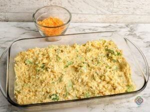 Cheddar broccoli cornbread batter in a casserole dish | Irish American Mom Broccoli cheddar cornbread batter spread evenly in a rectangular glass casserole dish, ready to be topped with shredded cheddar cheese and baked.