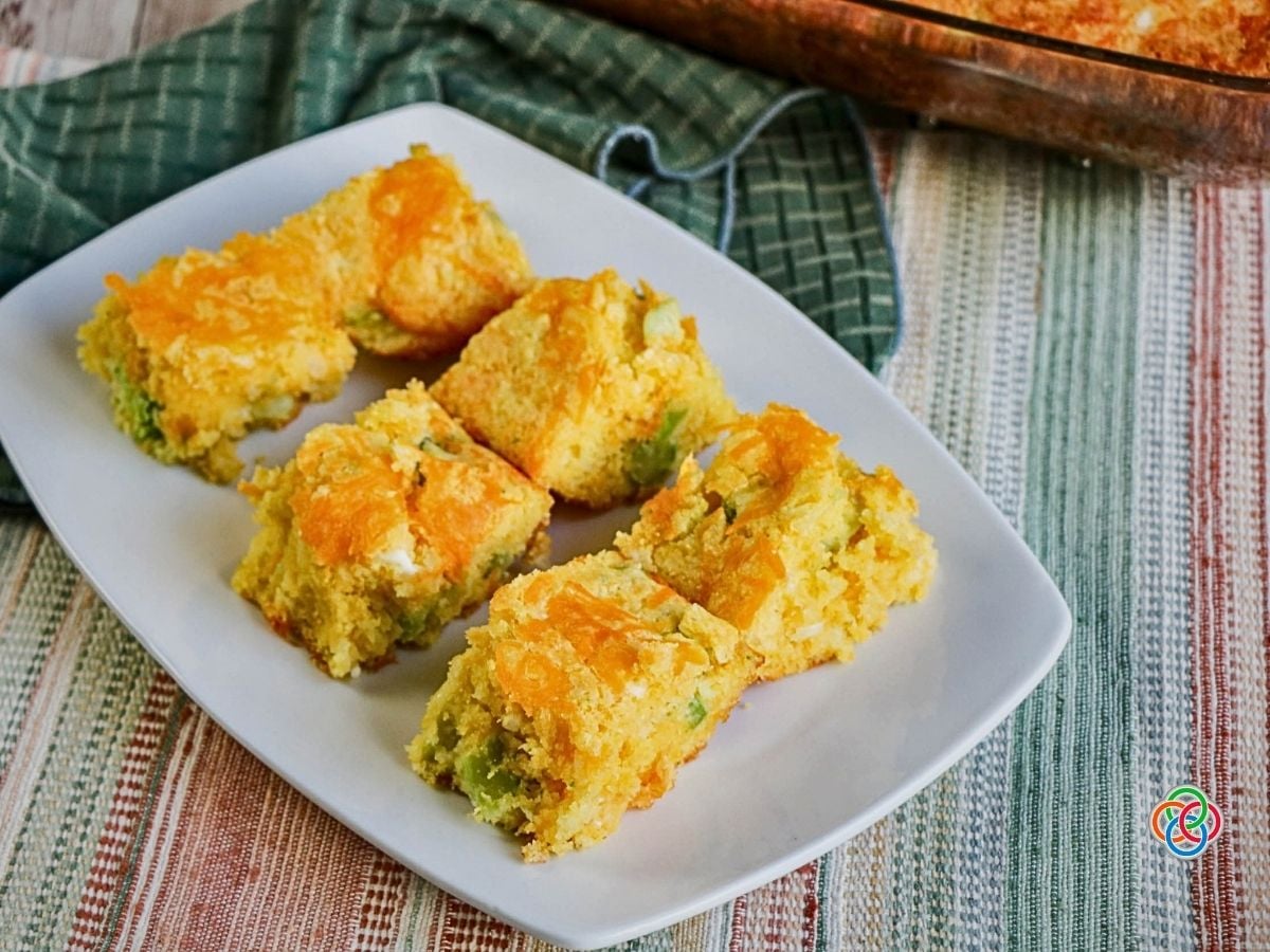 Cornbread with cheddar and broccoli | Irish American Mom Squares of golden broccoli cheddar cornbread arranged on a white serving platter, with melted cheese on top and green broccoli pieces visible throughout.