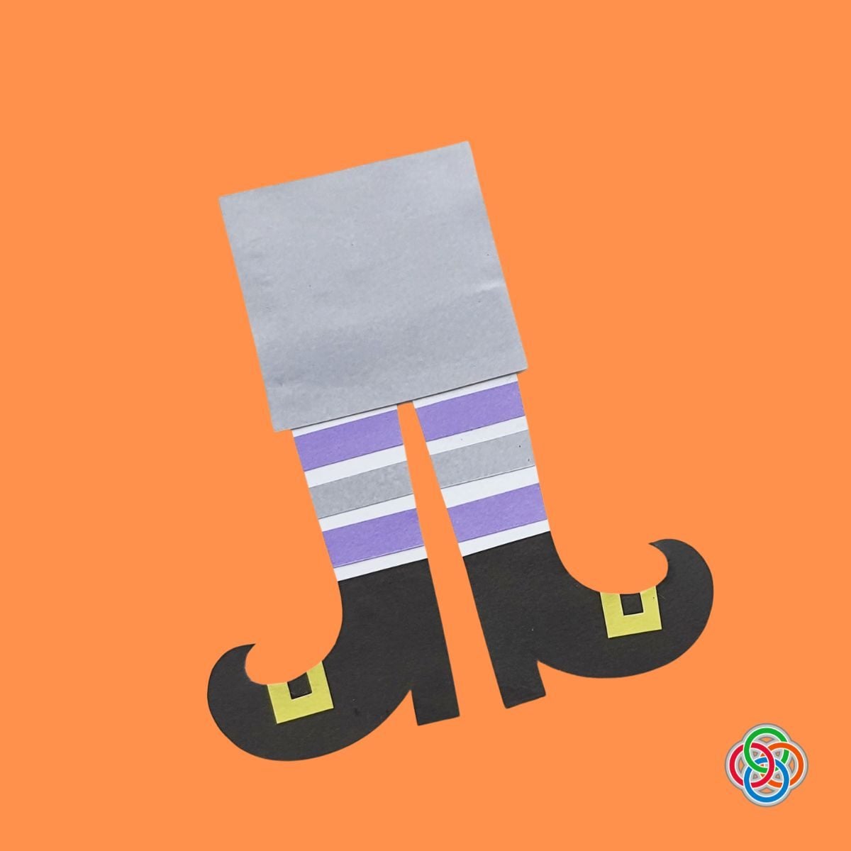 Creating a witch legs Halloween Bookmark | Irish American Mom Paper witch legs bookmark being assembled on an orange background, featuring purple, gray and white striped stockings, curly black witch shoes with yellow buckles, and a gray rectangular bookmark base.
