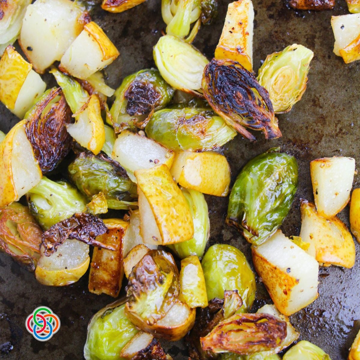 Crispy edges on roasted Brussels sprouts and pears with maple glaze | Irish American Mom Close-up of roasted Brussels sprouts and skin-on pear pieces with golden brown, crispy caramelized edges on a baking sheet.