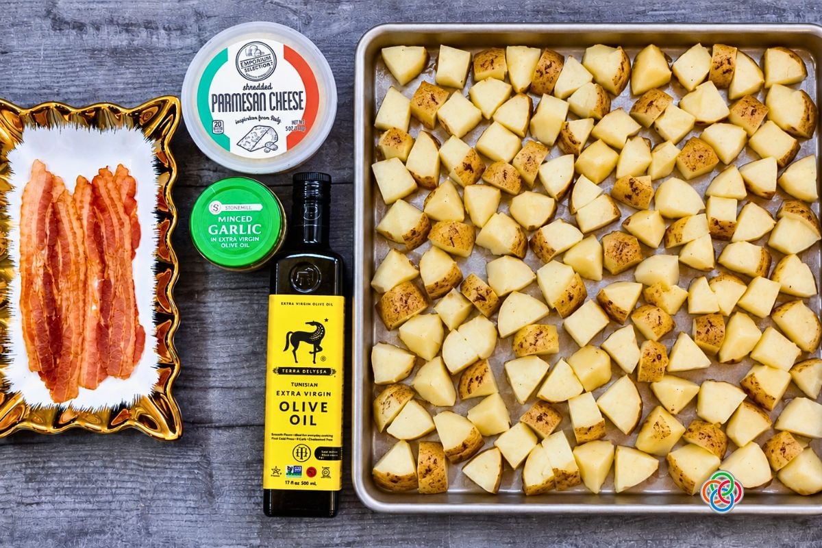 Cubed White Potatoes on a sheetpan for Bacon Parmesan Sheetpan Potatoes | Irish American Mom Cubed unpeeled white potatoes spread on a sheet pan beside bacon, Parmesan cheese, minced garlic and olive oil for making Bacon Parmesan Sheet Pan Potatoes.