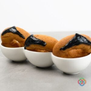 Three plain donuts in white bowls decorated with glossy black icing in a V-shaped widow's peak to create Dracula's hairline for a Halloween donut craft.