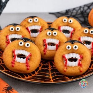 Halloween recipe graphic featuring Dracula donuts decorated with candy eyes, vampire fangs, black icing hair and dripping red icing on a black and orange spiderweb plate.