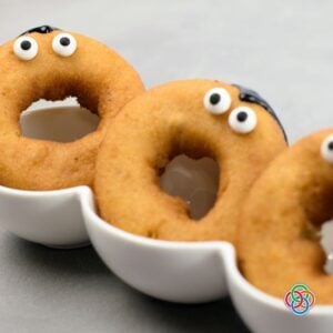 Plain golden donuts decorated with candy eyeballs and black icing hairlines as part of an easy Dracula donut Halloween decorating project.