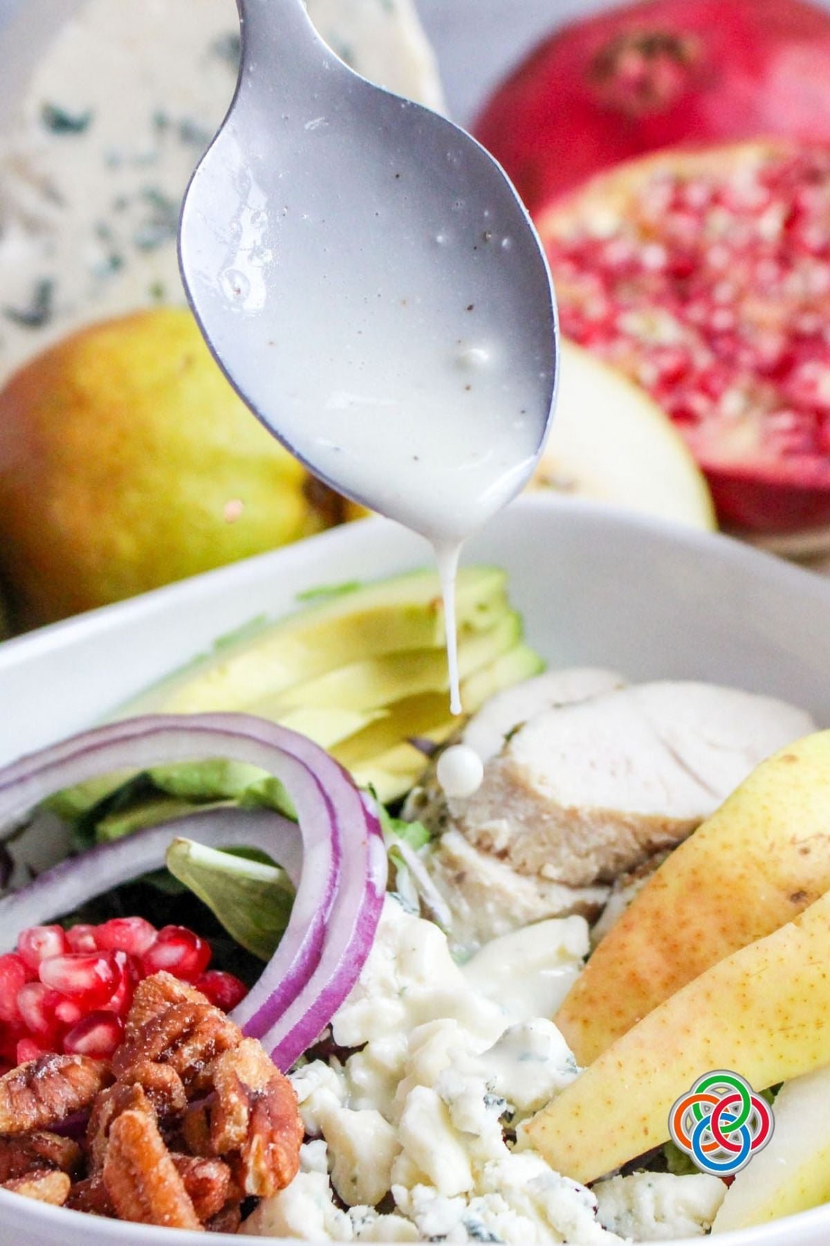 Fall or Harvest Pear Salad topped with Gorgonzola Dressing | Irish American Mom Creamy homemade Gorgonzola dressing being drizzled over a harvest pear salad with turkey, sliced pears, avocado, red onion, pomegranate seeds, honey-roasted pecans and crumbled Gorgonzola cheese.