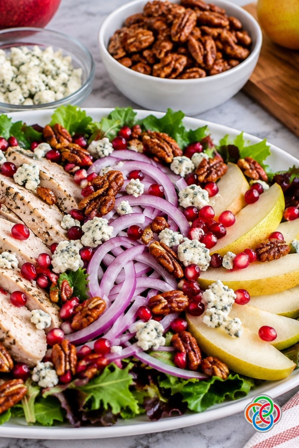 Fall or Harvest Pear Salad with pecans and pomegranate seeds | Irish American Mom Close-up of a fall harvest pear salad with sliced pears, turkey, red onion, mixed greens, pomegranate seeds, crumbled Gorgonzola cheese and honey-roasted pecans.
