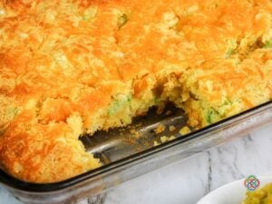 Freshly baked golden topped cheddar broccoli cornbread with a piece removed from th | Irish American Mom Freshly baked broccoli cheddar cornbread in a glass casserole dish with one piece removed, revealing the moist golden interior with broccoli and cheese beneath a melted cheddar topping.
