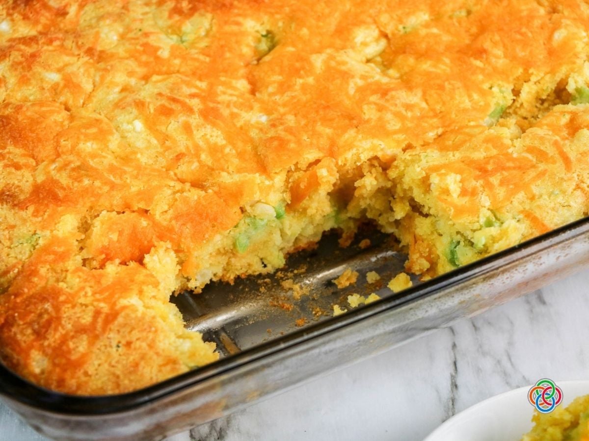 Freshly baked golden topped cheddar broccoli cornbread with a piece removed from th | Irish American Mom Freshly baked broccoli cheddar cornbread in a glass casserole dish with one piece removed, revealing the moist golden interior with broccoli and cheese beneath a melted cheddar topping.