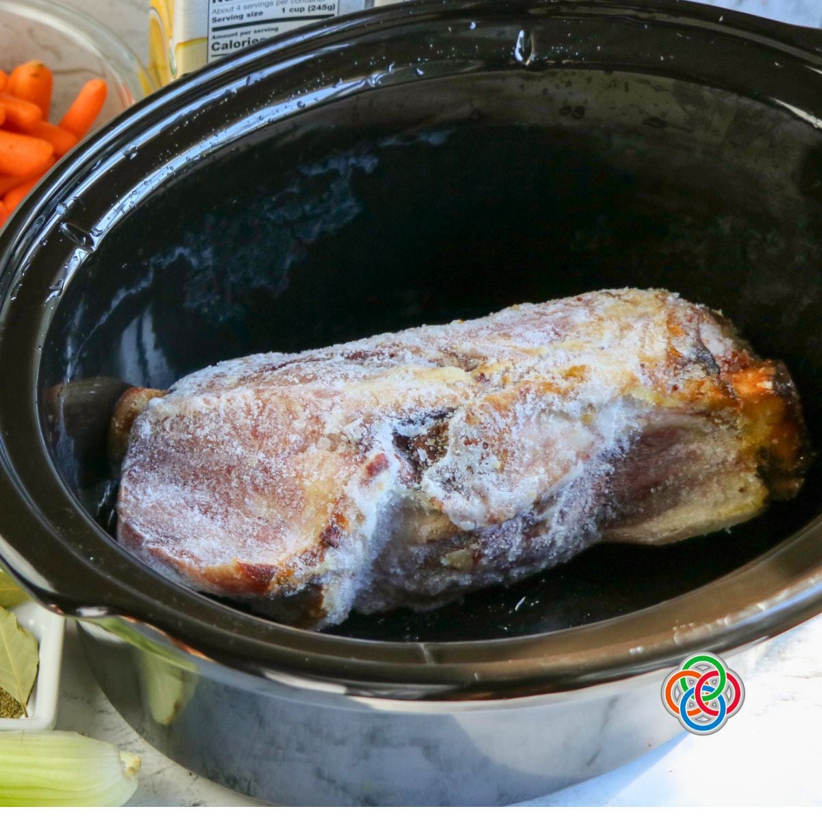 Ham bone in a crock pot | Irish American Mom Meaty leftover ham bone placed in a black slow cooker ready to make homemade ham bone and vegetable soup.