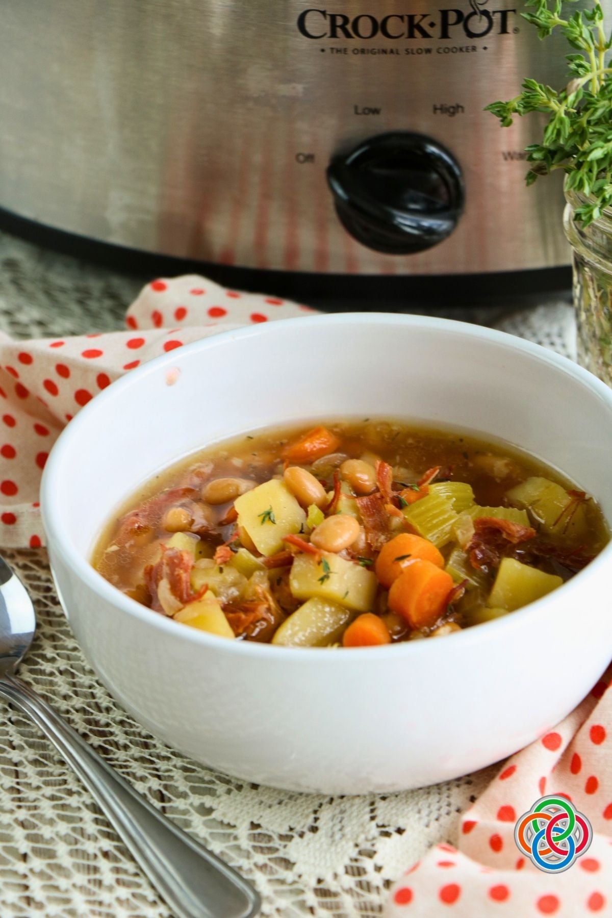 Homemade Crockpot Ham Bone Soup | Irish American Mom Bowl of homemade slow cooker ham bone soup with potatoes, carrots, celery, white beans and shredded ham, served beside a Crock-Pot.