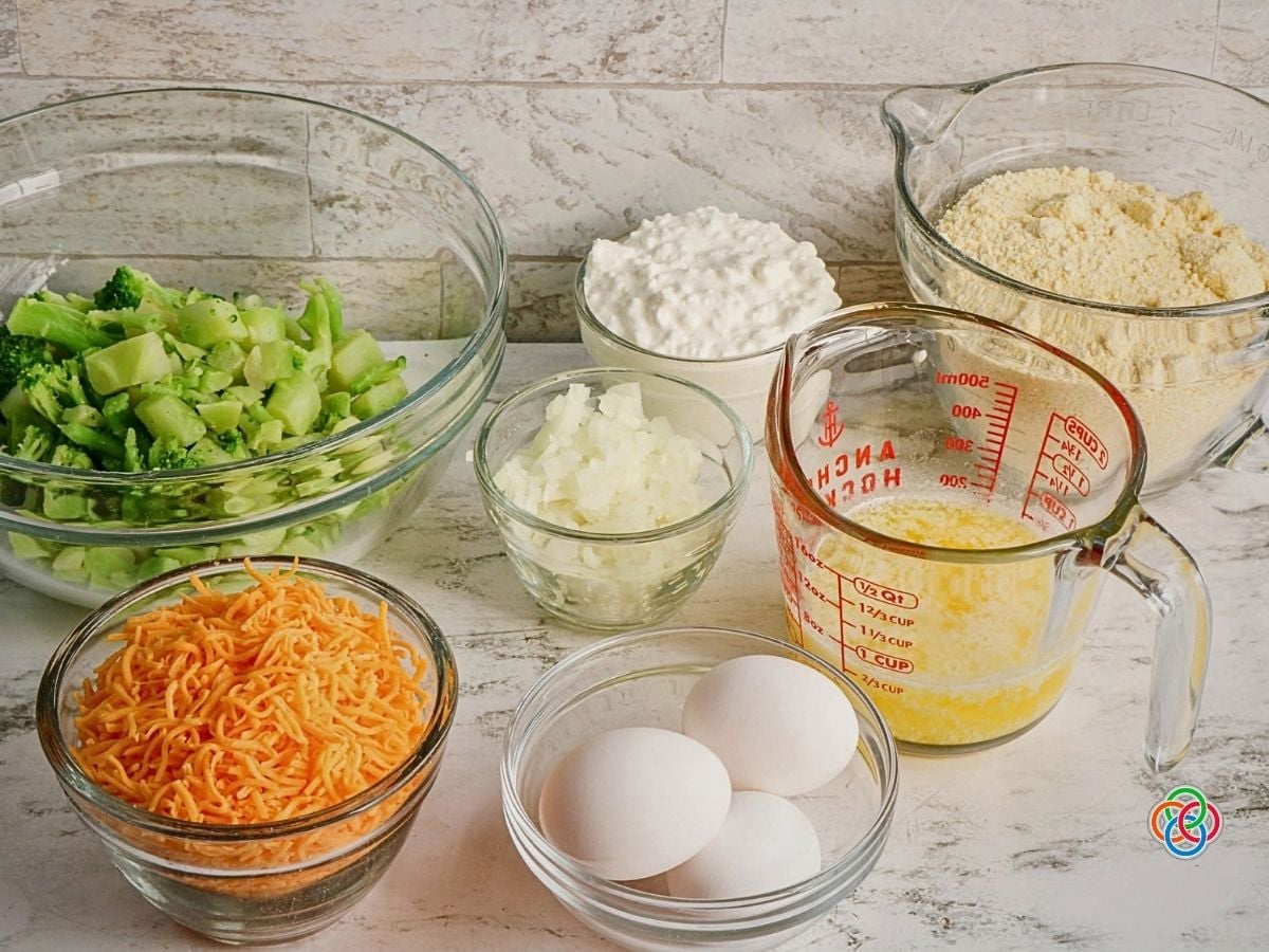 Ingredients for cheddar broccoli cornbread | Irish American Mom Ingredients for cheesy broccoli cornbread arranged in glass bowls, including chopped broccoli, shredded cheddar cheese, cottage cheese, chopped onion, eggs, melted butter and cornbread mix.