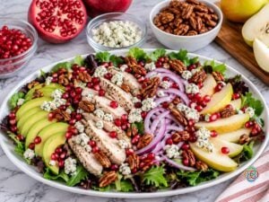 Pear Harvest Salad Sprinkled with Pomagranate Seeds and Pecans | Irish American Mom Harvest pear salad on a white platter with sliced pears, turkey, avocado and red onion, topped with pomegranate seeds, crumbled Gorgonzola cheese and honey-roasted pecans.