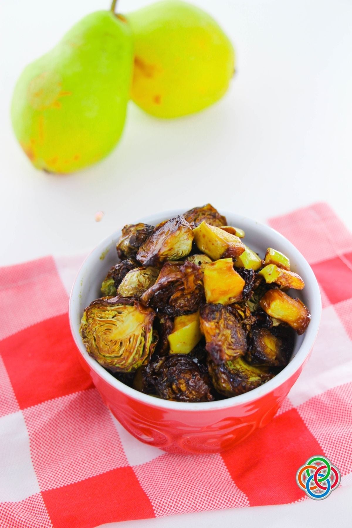 Roasted Brussels Sprouts and Pears | Irish American Mom Crispy roasted Brussels sprouts and golden pear pieces with maple Dijon glaze served in a red bowl on a red and white checkered cloth, and pears in the background