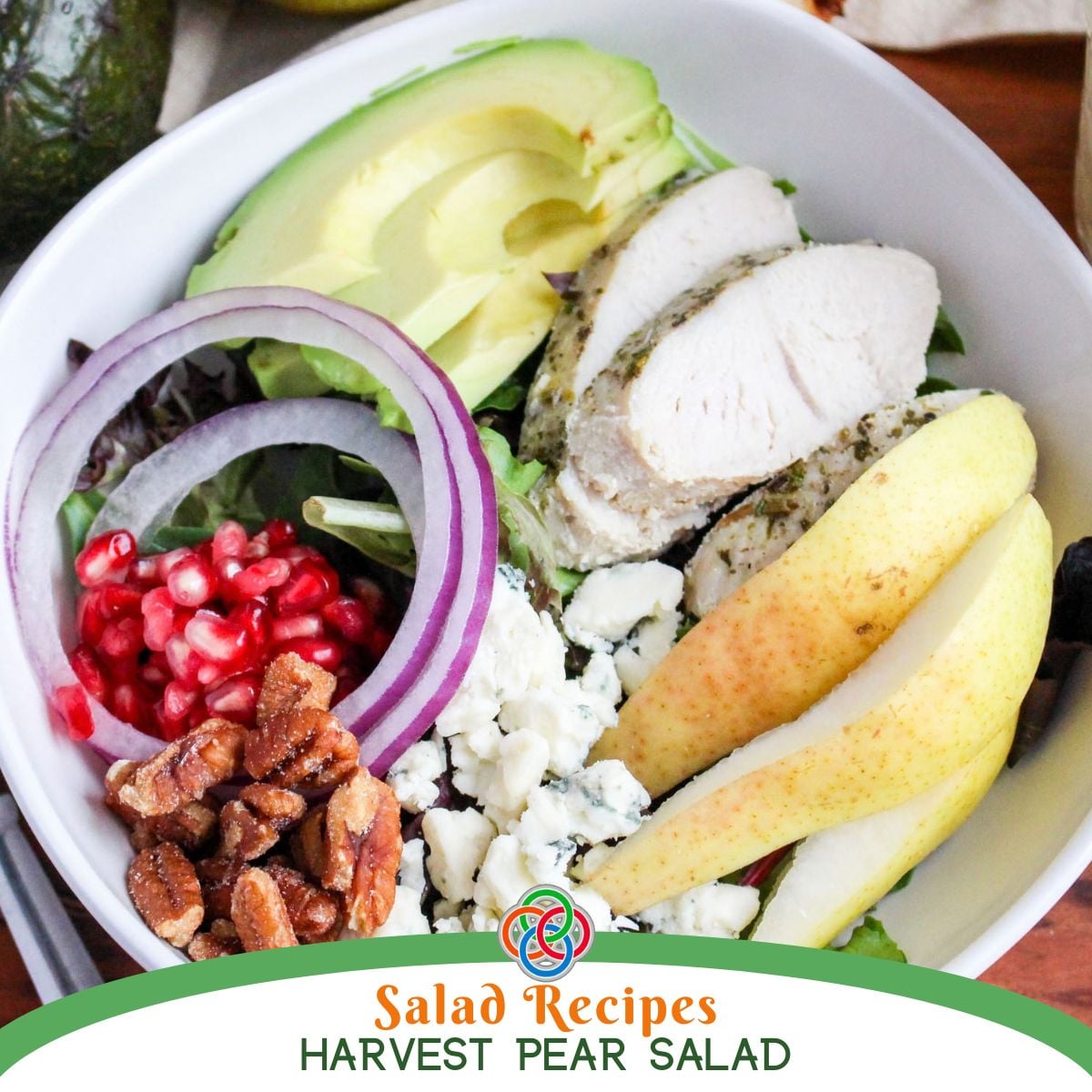 Harvest Pear Salad with sliced pears, turkey, avocado, red onion, pomegranate seeds, Gorgonzola cheese and pecans over mixed greens, with Harvest Pear Salad text.