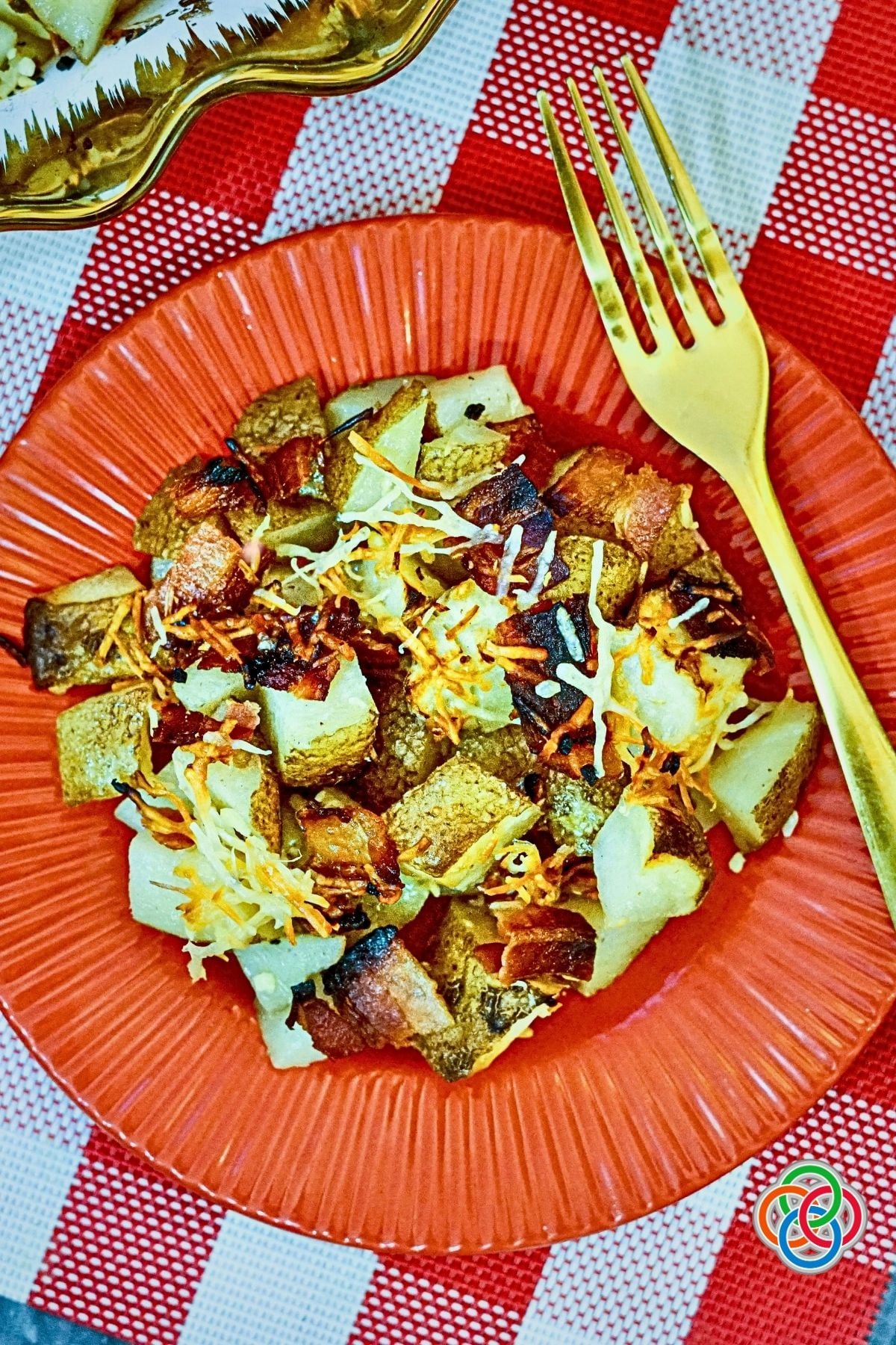 Serving of Parmesan Bacon Roast Potatoes on a Red Plate | Irish American Mom Crispy Bacon Parmesan roasted potatoes with garlic and golden melted cheese served on a red plate with a gold fork.