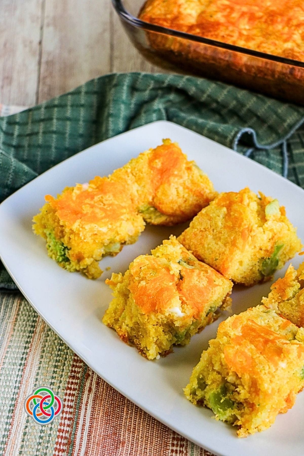 Servings of cheesy broccoli cornbread | Irish American Mom Golden squares of cheesy broccoli cornbread served on a white platter, showing pieces of green broccoli throughout and melted cheddar cheese baked on top.