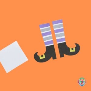 Striped witch legs and pointy shoes for a Halloween Bookmark | Irish American Mom Handmade paper witch legs with purple, gray and white striped stockings, black pointy curled shoes and yellow buckles, ready to be assembled into a Halloween bookmark.